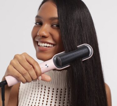 Woman running a heated styling tool through long hair, showing how the best hair straightening brush works in one pass