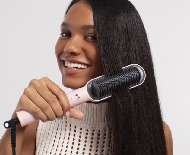 Woman running a heated styling tool through long hair, showing how the best hair straightening brush works in one pass