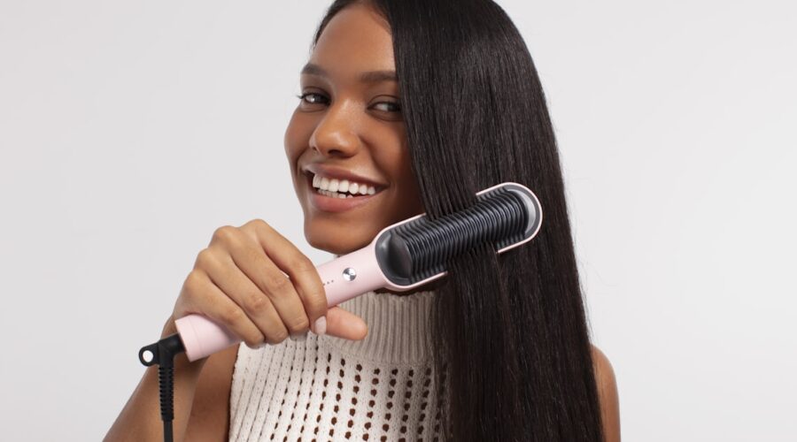 Woman running a heated styling tool through long hair, showing how the best hair straightening brush works in one pass
