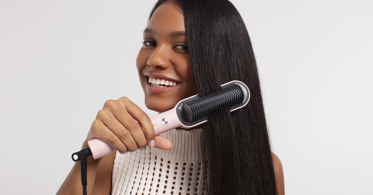 Woman running a heated styling tool through long hair, showing how the best hair straightening brush works in one pass
