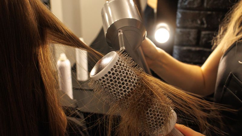 Hot air brush being used to shape a section of hair, the technique behind a volumizing blowout