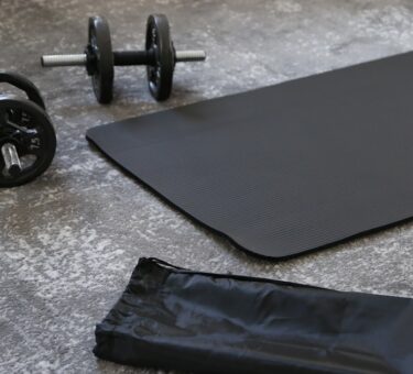 A black budget yoga mat with dumbbells and a carrying strap, ready for a home workout
