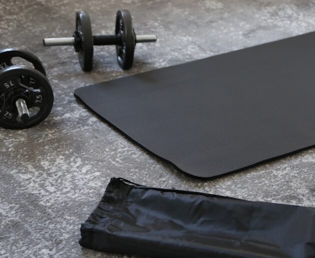 A black budget yoga mat with dumbbells and a carrying strap, ready for a home workout