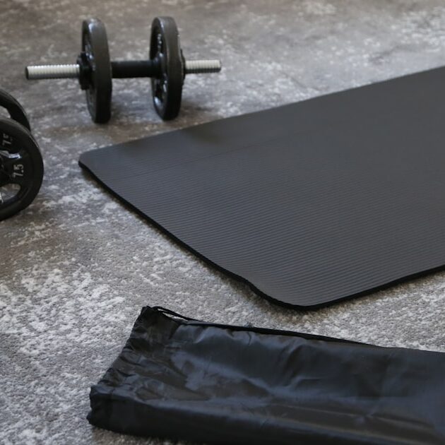 A black budget yoga mat with dumbbells and a carrying strap, ready for a home workout