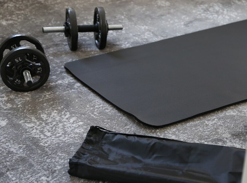 A black budget yoga mat with dumbbells and a carrying strap, ready for a home workout