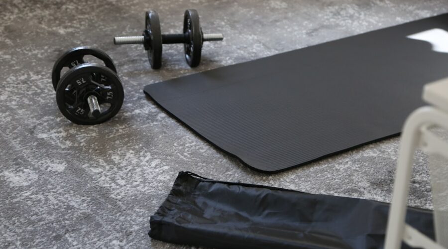 A black budget yoga mat with dumbbells and a carrying strap, ready for a home workout