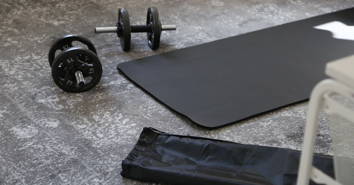 A black budget yoga mat with dumbbells and a carrying strap, ready for a home workout
