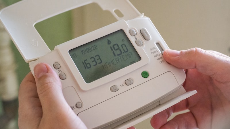 Hands holding an older programmable thermostat unit, the kind a budget programmable thermostat no c wire model replaces