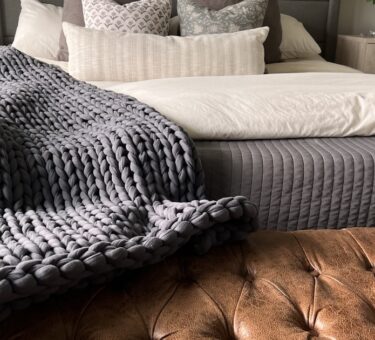 Chunky knit weighted blanket draped at the foot of a bed, one style of affordable weighted blanket for adults