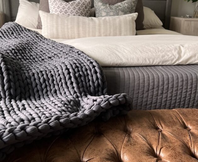 Chunky knit weighted blanket draped at the foot of a bed, one style of affordable weighted blanket for adults
