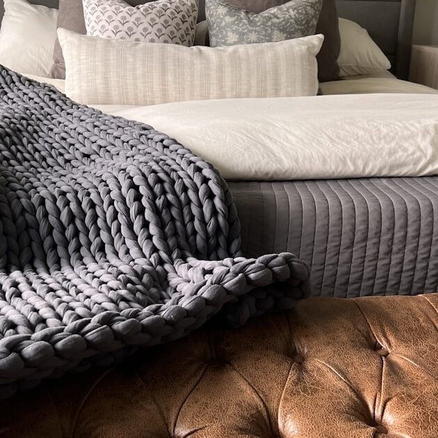 Chunky knit weighted blanket draped at the foot of a bed, one style of affordable weighted blanket for adults