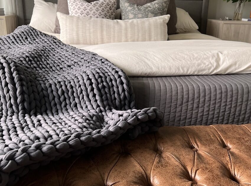 Chunky knit weighted blanket draped at the foot of a bed, one style of affordable weighted blanket for adults