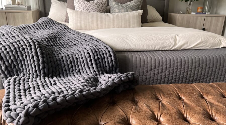 Chunky knit weighted blanket draped at the foot of a bed, one style of affordable weighted blanket for adults