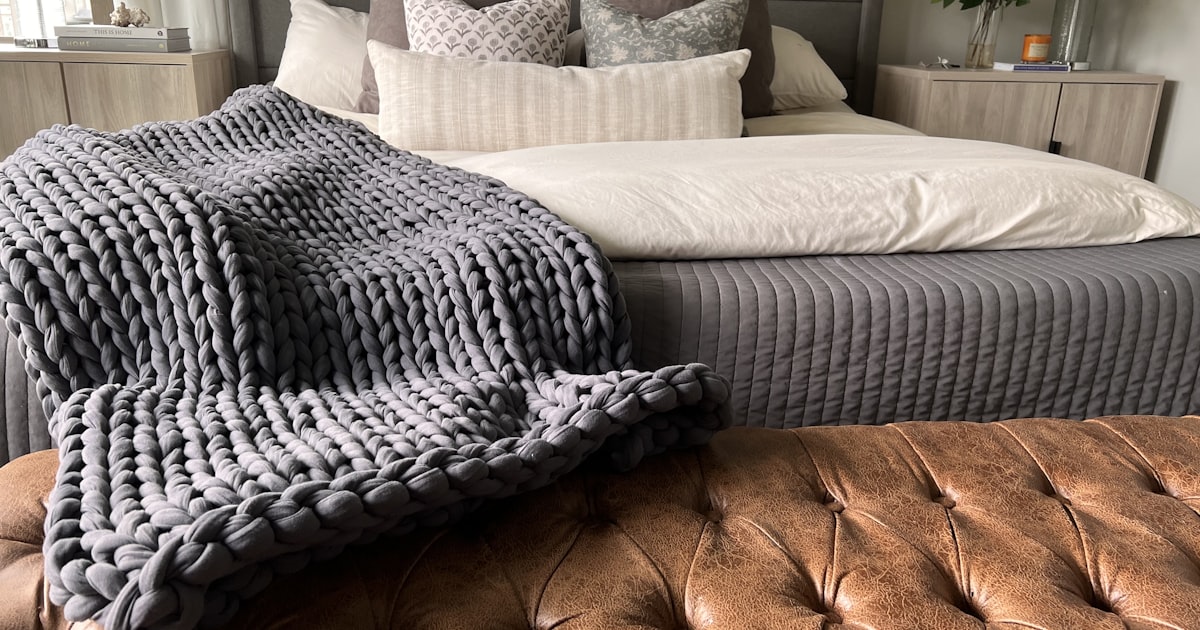 Chunky knit weighted blanket draped at the foot of a bed, one style of affordable weighted blanket for adults