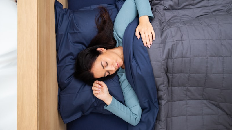 Person sleeping beside a grey quilted weighted blanket, the pocket stitching that keeps filling evenly spread