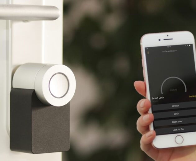 Silver smart lock installed on a front door with a smartphone app open showing lock and unlock controls
