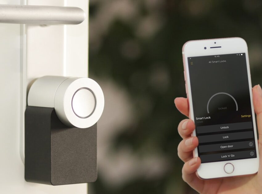 Silver smart lock installed on a front door with a smartphone app open showing lock and unlock controls