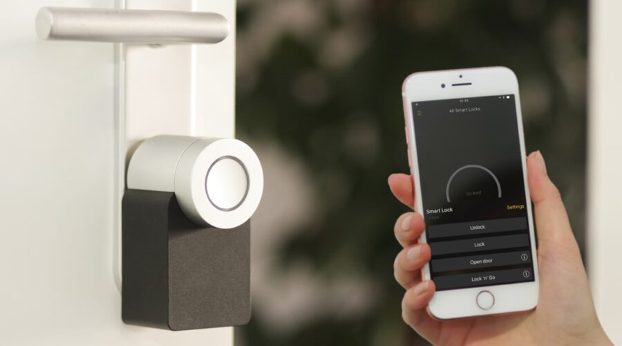Silver smart lock installed on a front door with a smartphone app open showing lock and unlock controls
