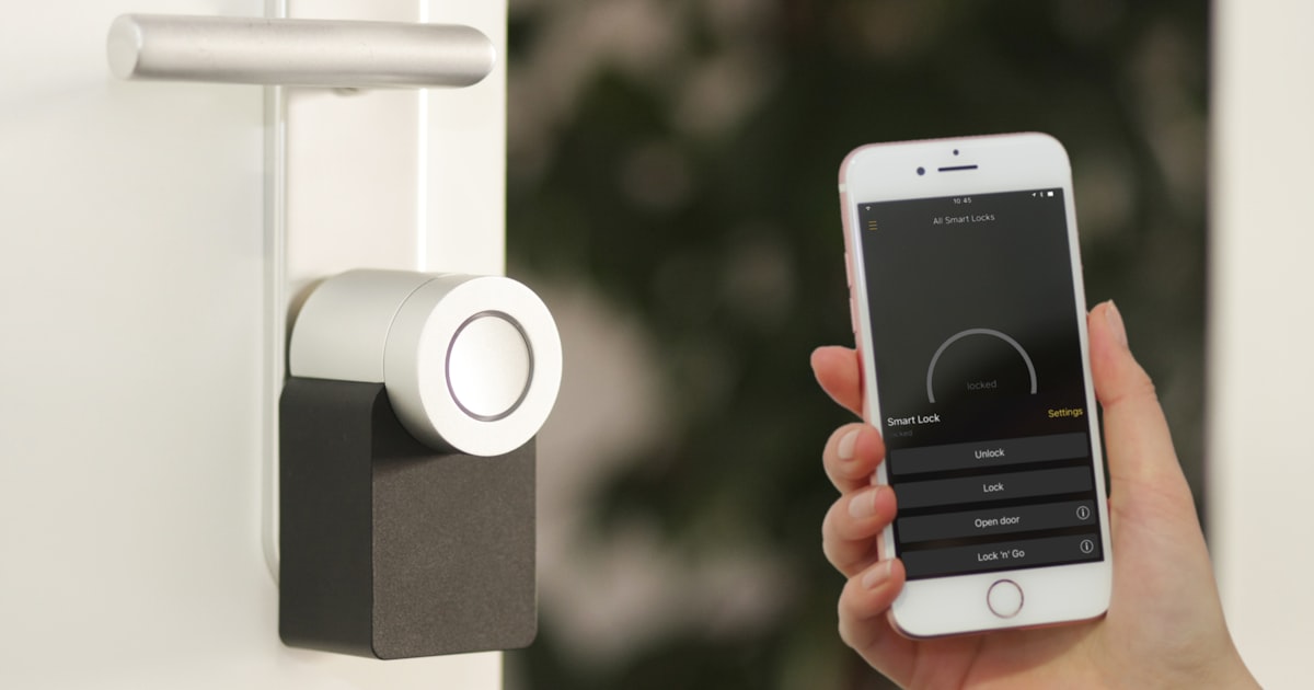 Silver smart lock installed on a front door with a smartphone app open showing lock and unlock controls