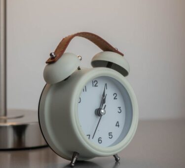Twin-bell clock beside a lit bedside lamp, illustrating sunrise alarm clock vs traditional alarm clock waking methods