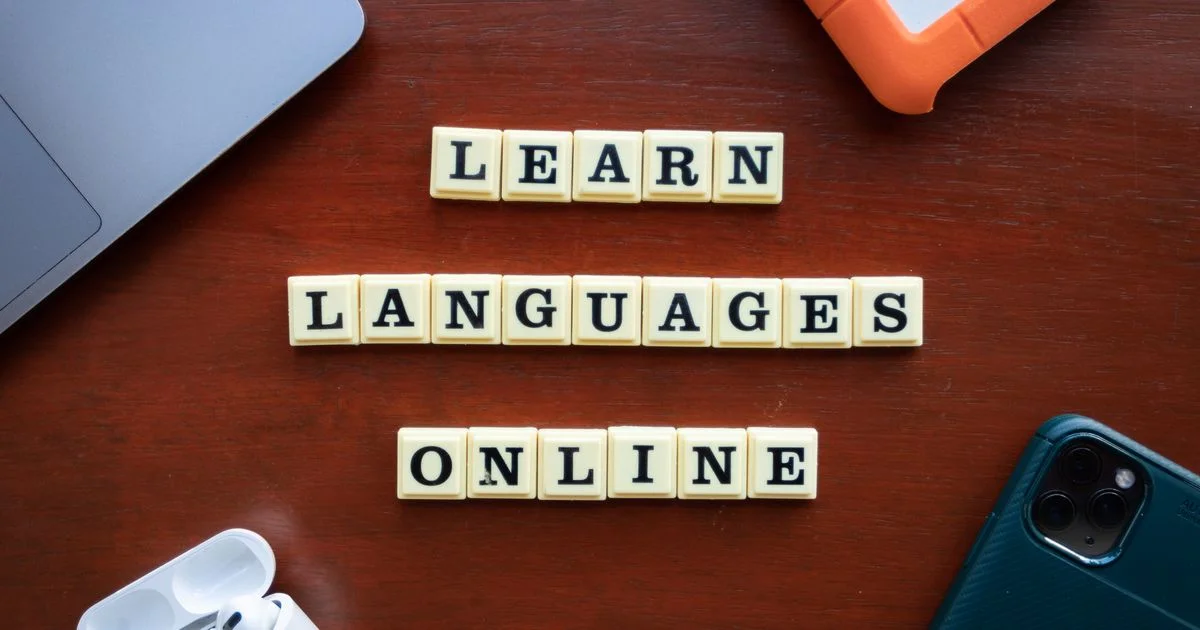 Letter tiles spelling learn languages online beside a laptop, phone and earbuds, the setup behind any language learning app for beginners