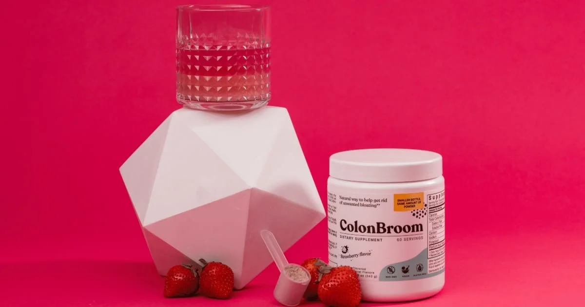 ColonBroom psyllium jar with a scoop of powder, a glass and strawberries, illustrating fiber supplement vs dietary fiber