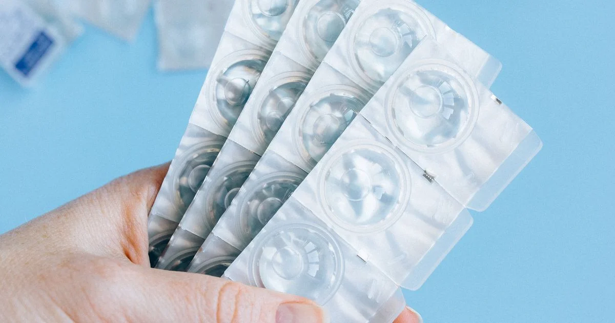 A hand holding unmarked blister packs of daily contact lenses, the product side of the contact lenses vs glasses comparison