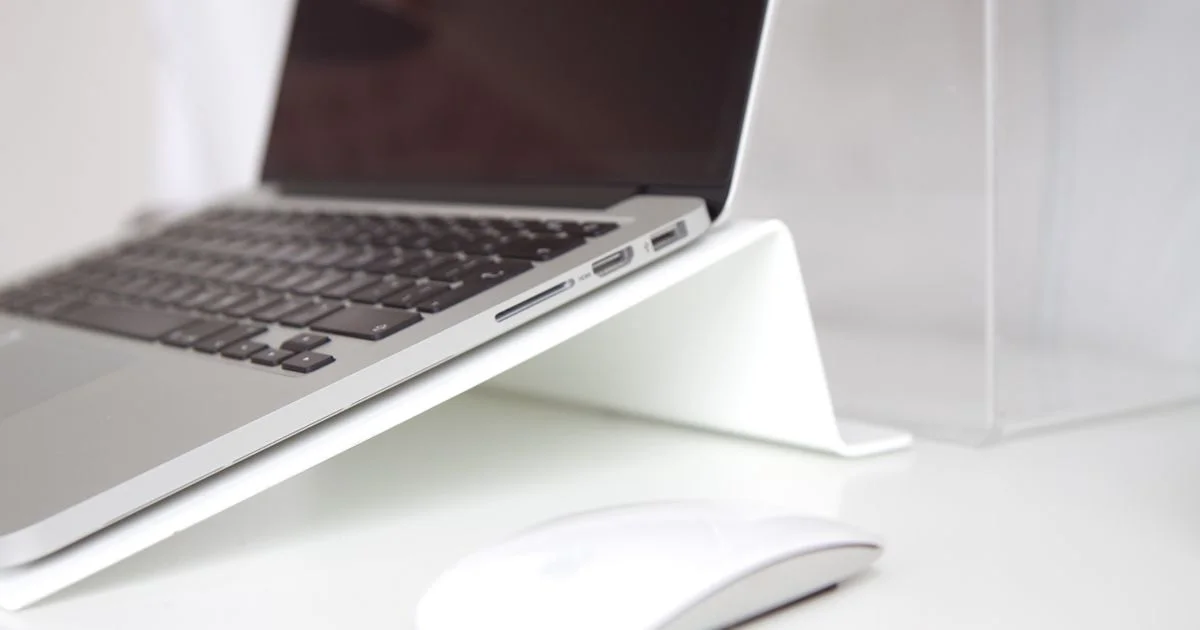 Laptop raised on a white ergonomic laptop stand on a desk beside a wireless mouse