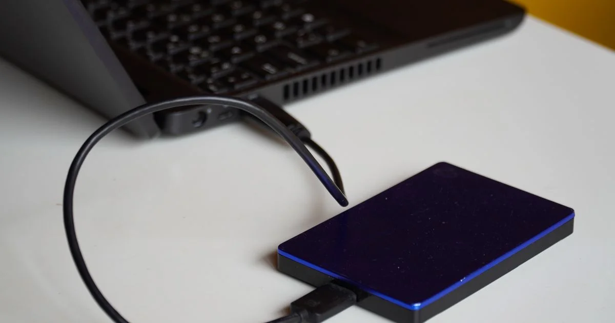Portable external hard drive for backup connected by USB cable to a laptop on a desk