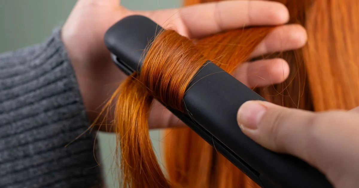 Close-up of flat iron plates clamped on a section of red hair, the heart of the flat iron or ceramic hair straightener question