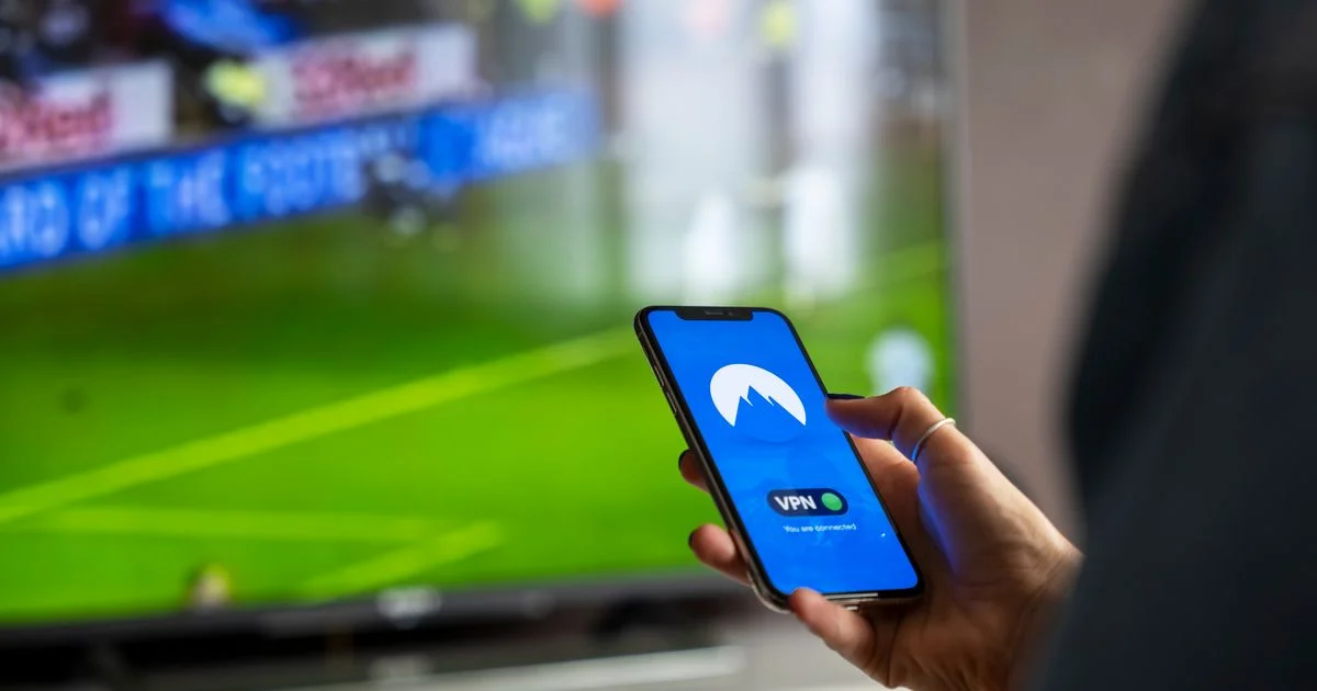 A phone showing a connected VPN app held in front of a TV streaming live sport, illustrating a free VPN trial for streaming