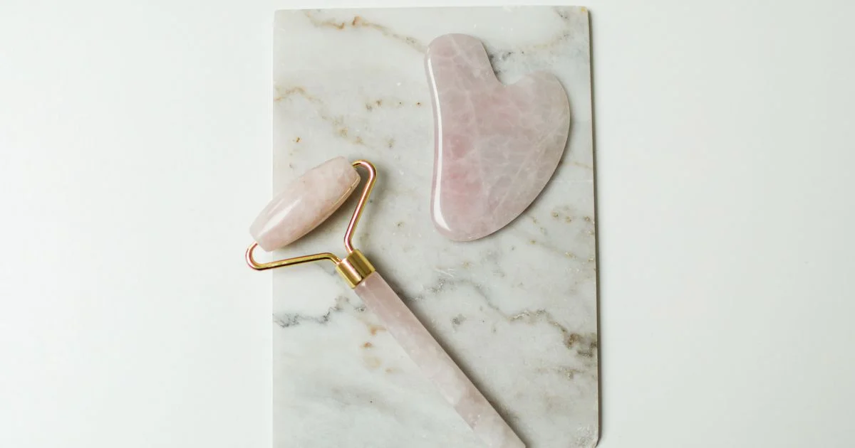 Rose quartz gua sha stone and jade roller side by side on marble, comparing the two facial tools