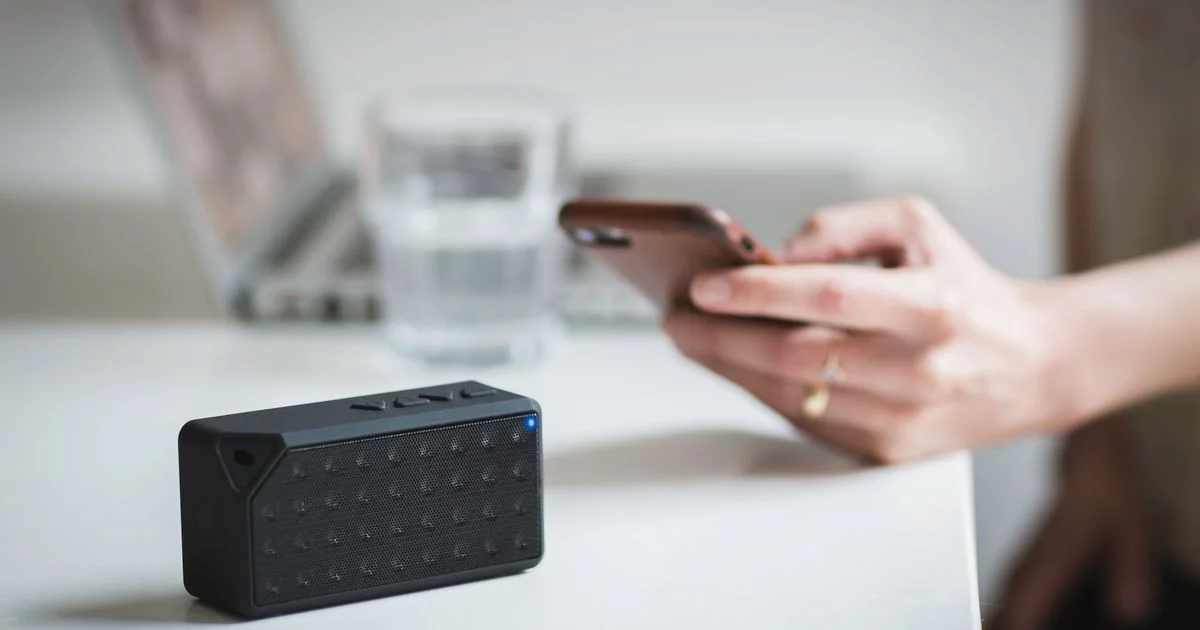 Unbranded portable Bluetooth speaker pairing with a phone on a desk, illustrating the JBL speaker vs Bose speaker spec comparison