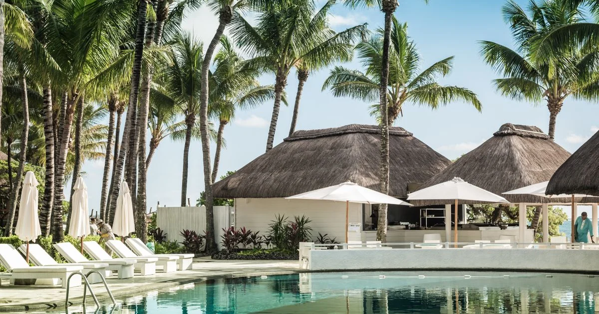 A resort pool with thatched cabanas and sun loungers, the kind of stay at issue in luxury vacation packages vs budget packages