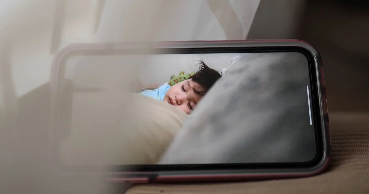 A baby monitor video feed showing a sleeping child on a phone screen, the everyday view behind the nanit vs owlet monitor comparison