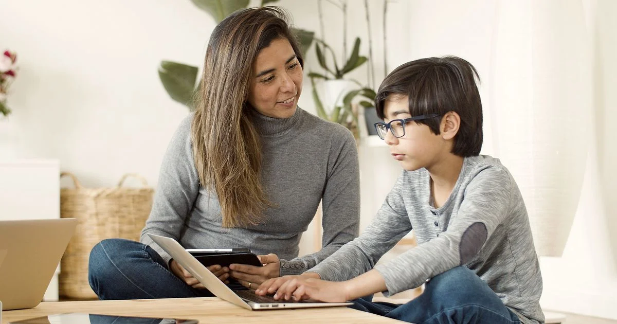 A parent helping a child set up a laptop and tablet at home, the moment a password manager for families gets adopted