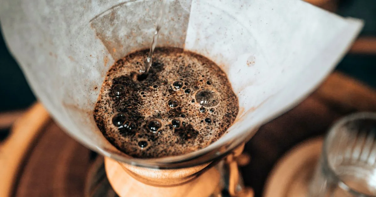 Hot water poured onto a bed of coffee grounds blooming in a paper filter, the gravity-driven side of the pour over coffee vs espresso machine comparison