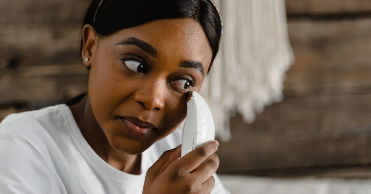 A woman holding a handheld facial toning device against her cheek, the at-home side of the radiofrequency vs microcurrent facial comparison