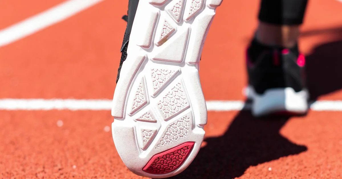 Close-up of an athletic shoe outsole with flex grooves and a rubber heel pad on a running track, the tread detail behind any running shoes vs walking shoes comparison