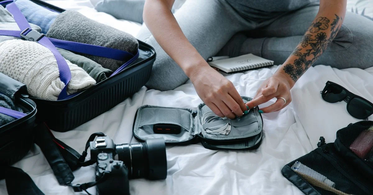 Traveler packing a cable organizer with a power bank and camera beside an open carry-on, showing small gadgets for travel packing