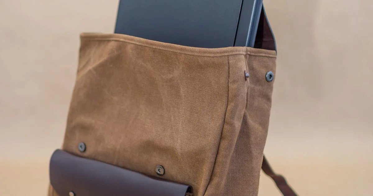A laptop sliding into the padded sleeve of a canvas backpack, the compartment layout that decides how a smart backpack with charging port is built