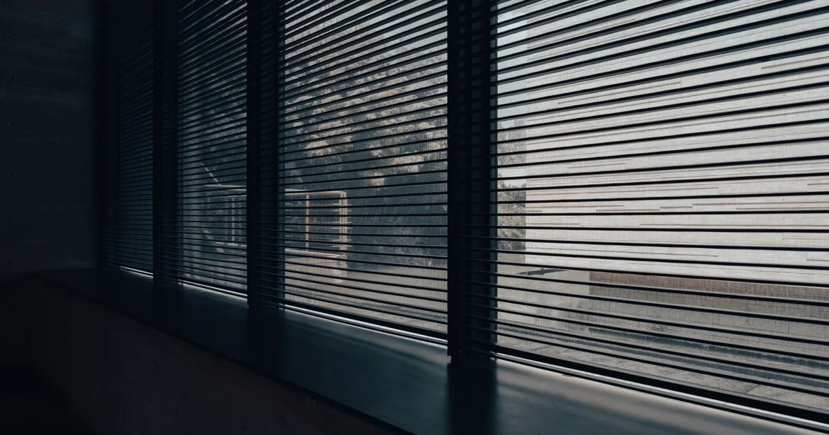 Slatted blinds filtering daylight across a window wall, illustrating the smart blinds vs curtains light-control comparison