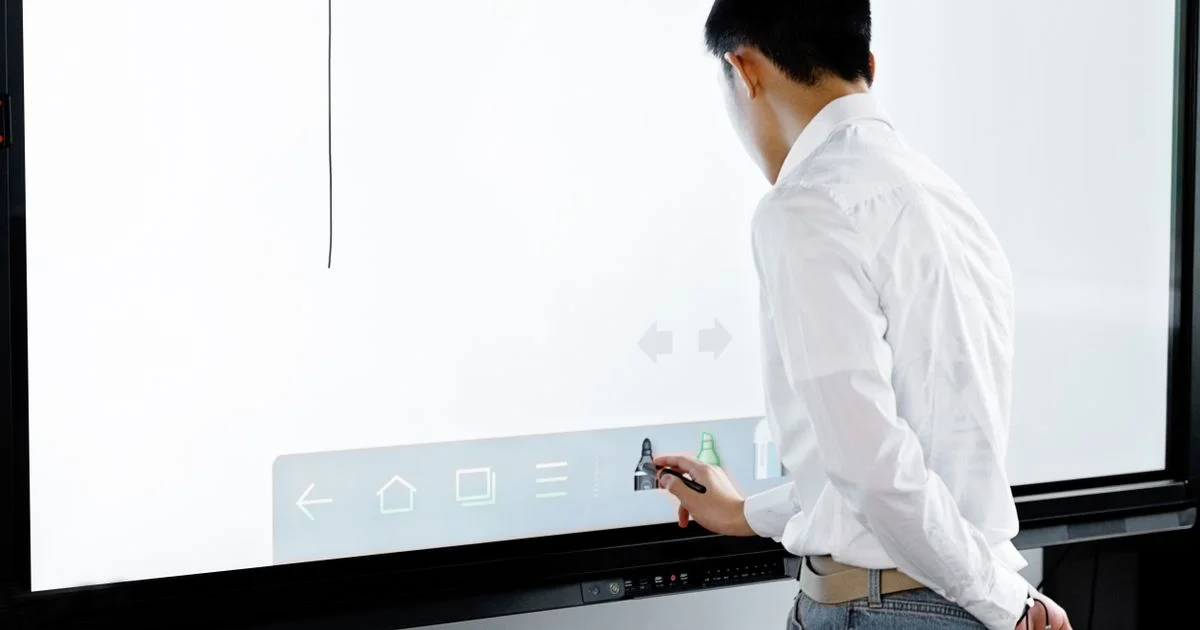 A hand using a stylus on a large interactive display, the smart board versus whiteboard comparison in an office