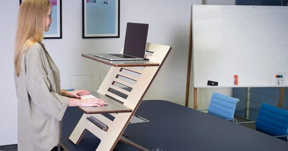Woman using a standing desk converter with a laptop on the upper platform and keyboard on the lower tray