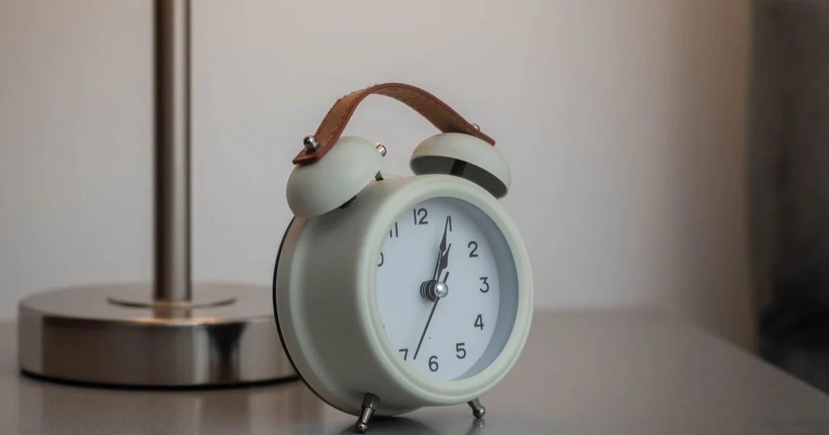 Twin-bell clock beside a lit bedside lamp, illustrating sunrise alarm clock vs traditional alarm clock waking methods